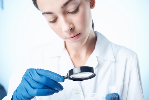 Asistente de laboratorio femenino en una bata blanca mirando a través de una lupa de investigación profesional