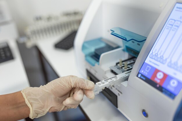 Asistente de laboratorio femenino haciendo análisis con tubos de ensayo y máquinas analizadoras sentadas en el moderno laboratorio técnico de laboratorio cargando muestras en un analizador químico