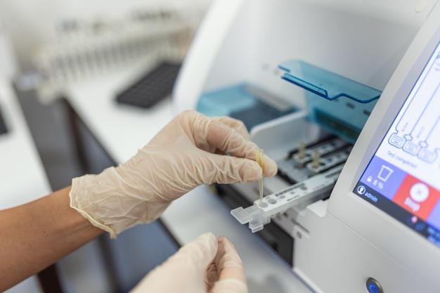 Asistente de laboratorio femenino haciendo análisis con tubos de ensayo y máquinas analizadoras sentadas en el moderno laboratorio técnico de laboratorio cargando muestras en un analizador químico