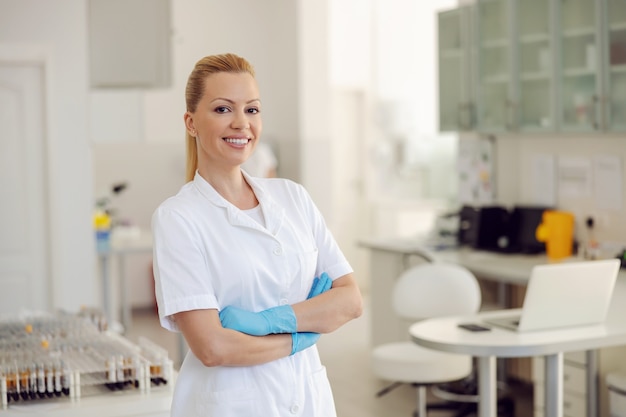 Asistente de laboratorio femenino de pie en el laboratorio con las manos cruzadas