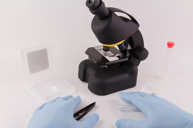 Un asistente de laboratorio con guantes médicos azules trabaja con un microscopio.