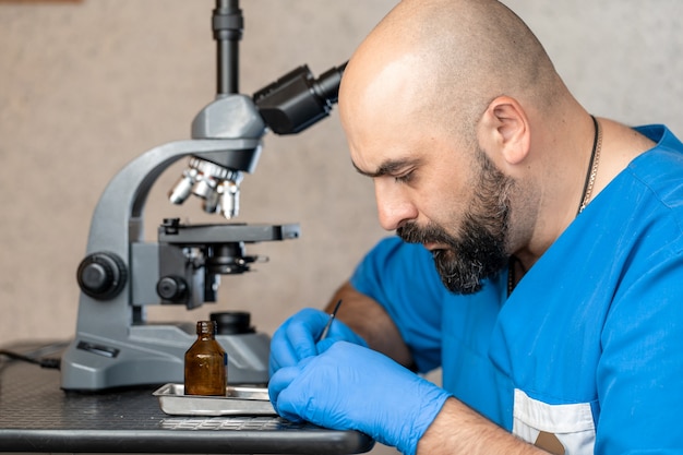 Asistente de laboratorio masculino examinar muestras de biomateriales en microscopio