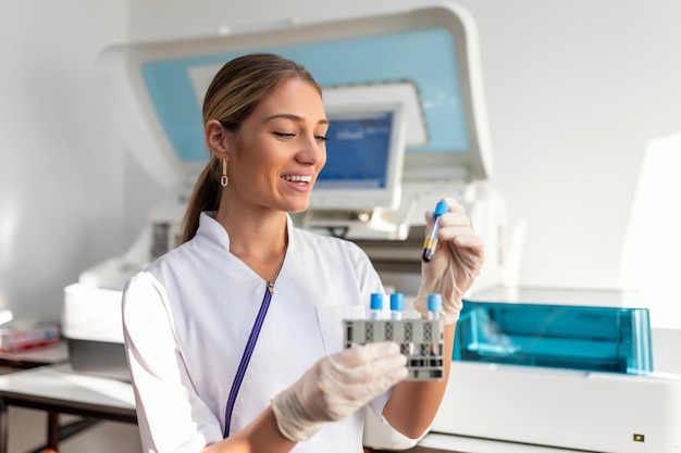 Foto asistente de laboratorio poniendo tubos de ensayo en el soporte médico científico mirando el tubo de ensayo de sangre trabajando en el experimento de bioquímica en el laboratorio del hospital de microbiología