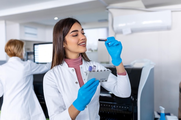 Asistente de laboratorio poniendo tubos de ensayo en el soporte Médico científico mirando el tubo de ensayo de sangre trabajando en el experimento de bioquímica en el laboratorio del hospital de microbiología