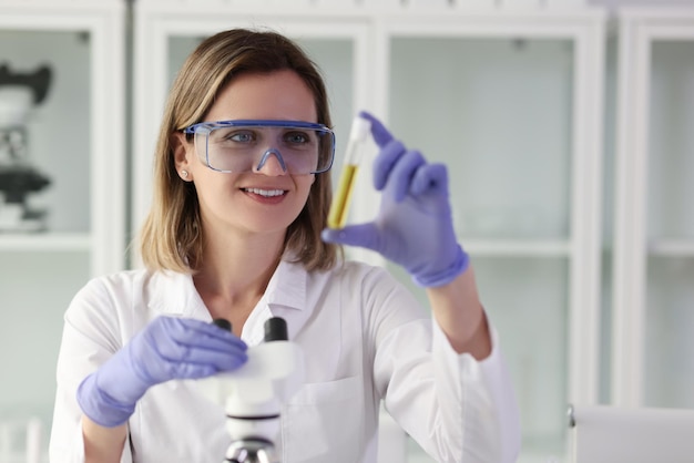 Un asistente de laboratorio sonriente con gafas protectoras examina una muestra de líquido amarillo en la prueba