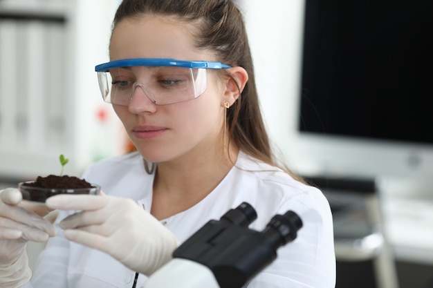 Asistente de laboratorio sostiene germen cerca del microscopio