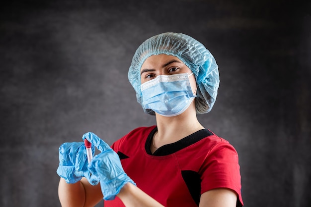 Asistente de laboratorio en uniforme rojo mirando muestras de sangre en un tubo de ensayo aislado en Covid-19 negro