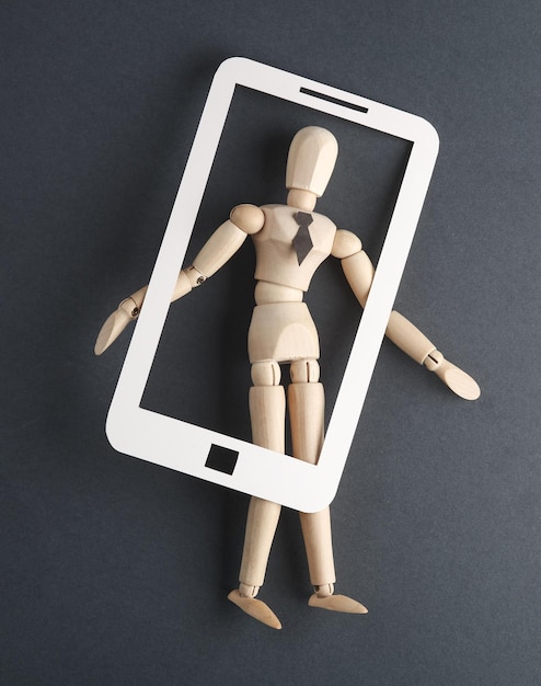 Asistente en línea Títere de madera con un teléfono inteligente recortado en papel sobre un fondo gris