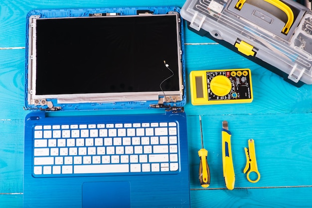 El asistente repara la computadora portátil con herramientas y manos en la vista superior de la mesa de madera azul