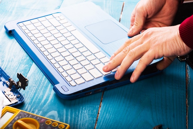 El asistente repara la computadora portátil con herramientas y manos en la vista superior de la mesa de madera azul