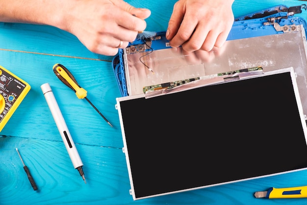 El asistente repara la computadora portátil con herramientas y manos en la vista superior de la mesa de madera azul