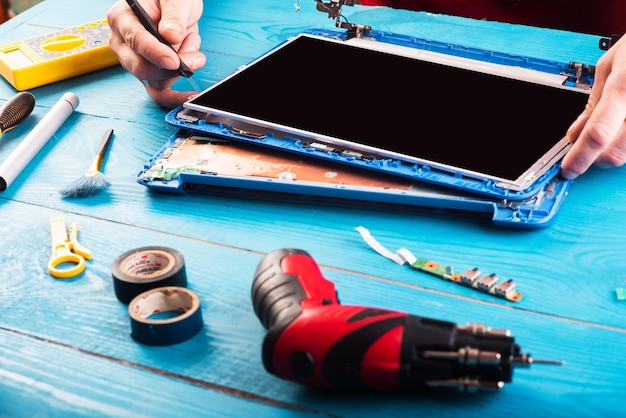 El asistente repara la computadora portátil con herramientas y manos en la vista superior de la mesa de madera azul