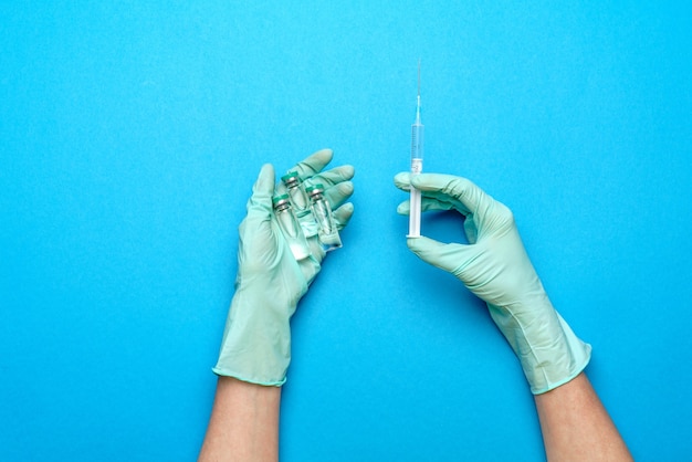 Asistente de técnico de laboratorio o médico con guantes de goma o látex sosteniendo una ampolla con medicamento o vacuna y jeringa