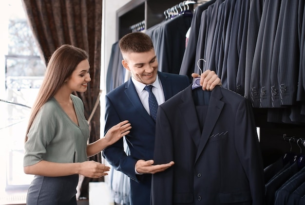 Asistente de tienda femenina ayudando al hombre a elegir traje en la tienda