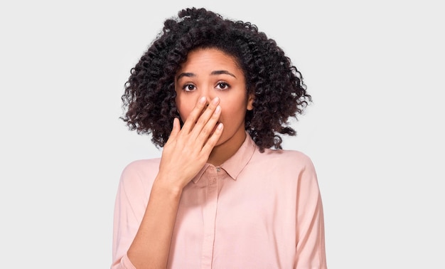 Asombrada mujer joven afroamericana tiene expresión asombrada Hermosa mujer afro escucha algo increíble mantiene las manos abiertas aisladas sobre fondo blanco Concepto de emociones