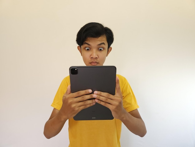 Asombrado hombre asiático feliz usando tableta digital mirando las noticias de las redes sociales hombre sorprendido