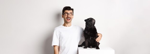 Asombrado joven con anteojos abrazando a su dueño de mascota y pug mirando la promoción de la esquina superior izquierda