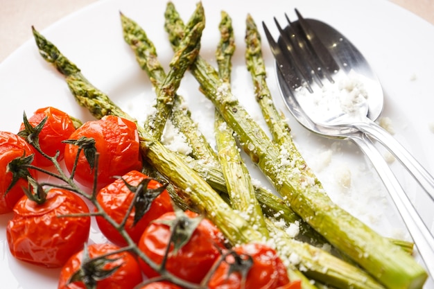 Aspargos cozidos e tomate cereja em um prato. Fechar-se.