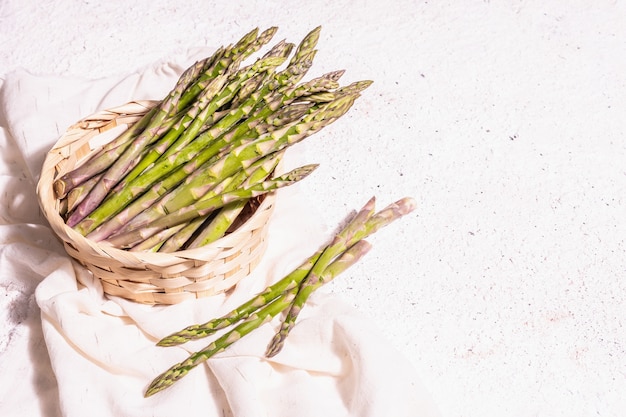 Aspargos maduros em uma cesta de vime. Ingredientes verdes frescos prontos para cozinhar alimentos saudáveis. Luz dura moderna, sombra escura. Fundo de gesso branco, copie o espaço