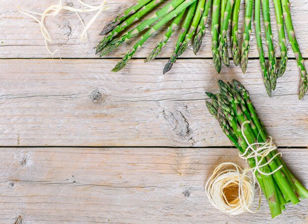 Aspargos orgânicos verdes frescos e um rolo de linha em uma mesa de madeira velha