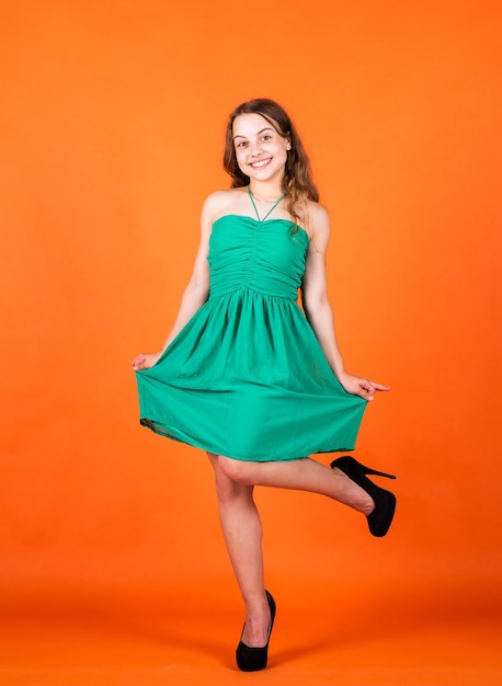 Aspecto elegante de moda. hermosa chica adolescente con pelo largo y rizado. estilo de moda infantil. belleza natural femenina. infancia feliz. niño lindo sobre fondo naranja. salón de peluquería. Humor positivo.