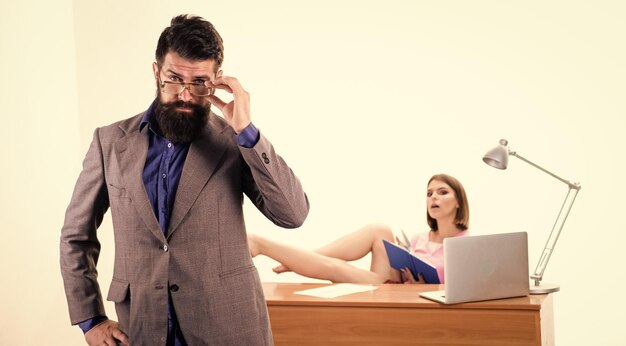Foto un aspecto intelectual de hipster hipster arreglando sus gafas mientras mujer sexy trabajando en el fondo hipster barbudo y bonito compañero de trabajo en la oficina hipster con barba larga en estilo casual de negocios
