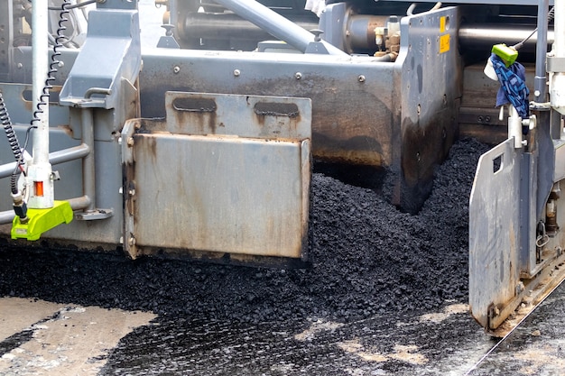 Asphaltfertiger auf der Straße beim Verlegen von Asphalt, ein Teil des Autos hautnah. Straßenreparatur. Eine neue Straße bauen