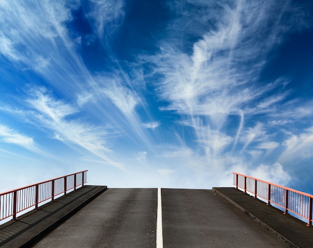 Asphaltstraße, die mit Wolken in den Himmel geht