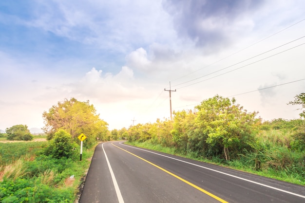 Asphaltstraße durch das grüne Feld und Wolken auf blauem Himmel am Sommertag