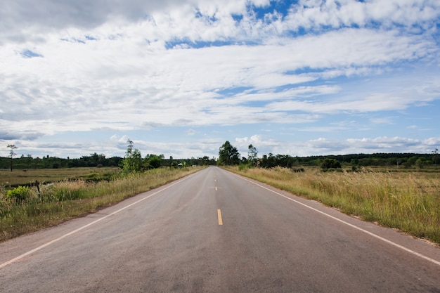 Asphaltstraße durch das Reisfeld und Wolken am blauen Himmel