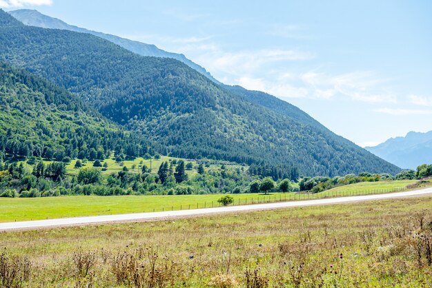 Asphaltstraße und grüne Felder mit Bergen unter blauem Himmel