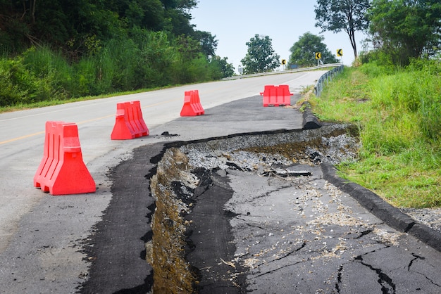 Asphaltstraße zusammengebrochen und Risse am Straßenrand, Road Erdrutsch mit Kunststoffsperren auf bergauf nachlassen