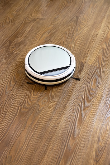 Aspirador de pó de robô sem fio redondo branco em piso laminado marrom