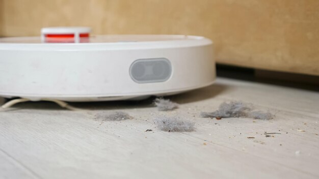 La aspiradora robot se pasea por el suelo y recoge polvo cerca del sofá en la sala de estar