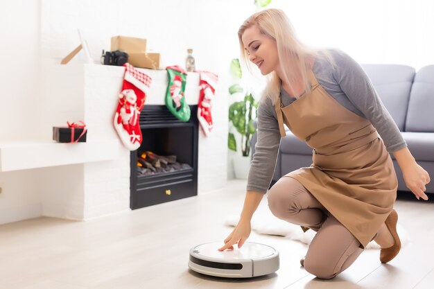 Aspiradora robótica sobre suelo de madera laminada con tecnología de limpieza inteligente. Árbol de navidad