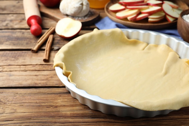 Assadeira com massa crua para torta de maçã e ingredientes na mesa de madeira