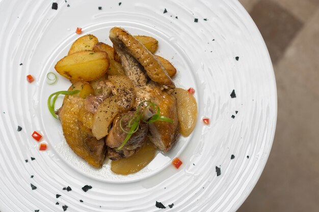 Assado de pintada com batatas, com ervas verdes, colocadas em um prato branco