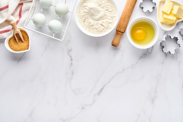 Assando fundo com farinha, ovos, utensílios de cozinha, utensílios e formas para biscoitos na mesa branca