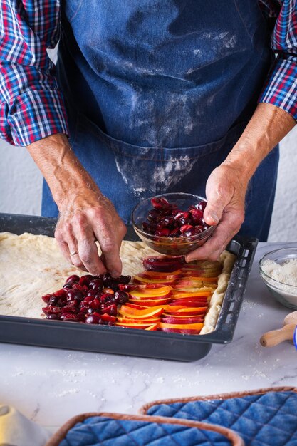 Assar comendo em casa comida saudável e conceito de estilo de vida Homem padeiro sênior cozinhando amassar massa fresca com as mãos rolando com pino espalhando o recheio na torta em uma mesa de cozinha com farinha