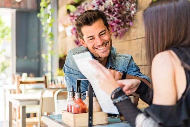 Assento feliz jovem casal em um restaurante, olhando para o menu