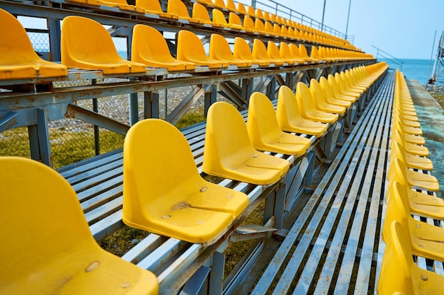 Assentos de plástico amarelo no pódio de um pequeno campo esportivo.