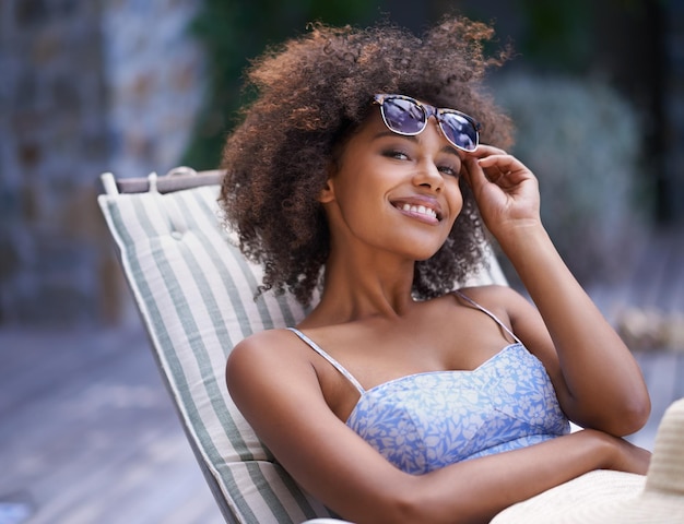 É assim que eu quero passar todos os dias Mulher étnica atraente relaxando na espreguiçadeira segurando seus óculos de sol