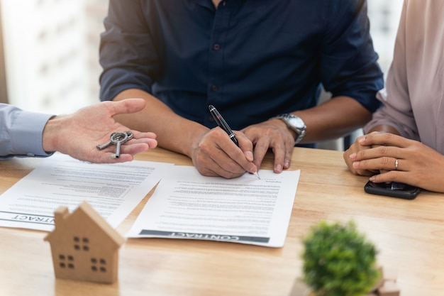 Foto assinando um contrato para a compra de casa no escritório do agente imobiliário e agente imobiliário dando a chave da casa nova para o jovem casal no escritório