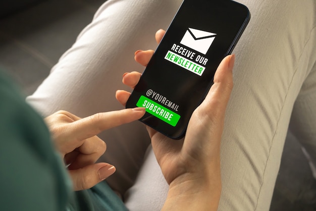 Assine o conceito de boletim informativo em um telefone celular ou smartphone. Mulher dentro de casa segurando um telefone celular com a página de inscrição no boletim informativo, inscreva-se e registre-se