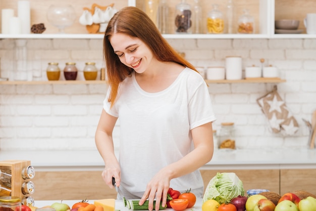 Assistência médica. Coma bem para estar em forma. Nutrição saudável e equilibrada. Sorrindo, jovem fêmea cortando legumes.