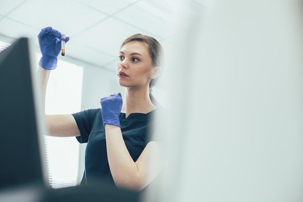 Assistente de laboratório calmo e curioso segurando um tubo de ensaio com amostra de sangue