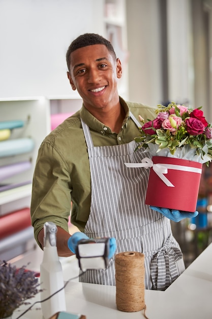 Foto assistente de loja de flores multirracial de excelente humor passando um dispositivo de digitalização para um comprador