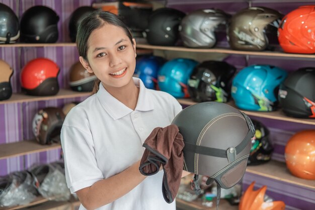 Assistente de loja de mulher sorridente limpando capacete com pano na loja de capacetes