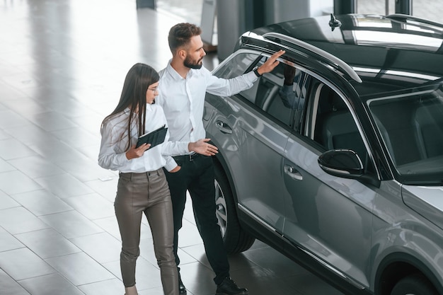 Foto assistente está ajudando o cliente homem com mulher em roupas brancas estão juntos na concessionária