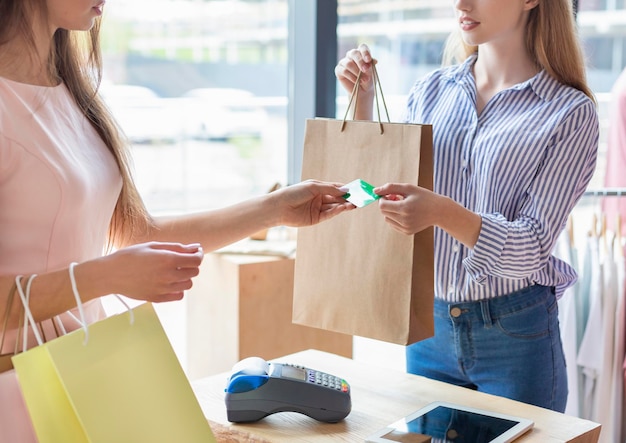 Foto assistente feminina caucasiana segurando compras, aceitando cartão de crédito do cliente, interior da loja